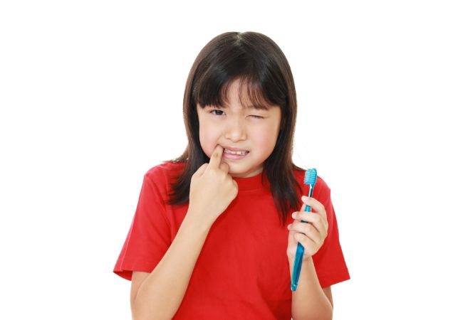 左手に歯ブラシを持ち、右手で奥歯を触る赤い服の女の子