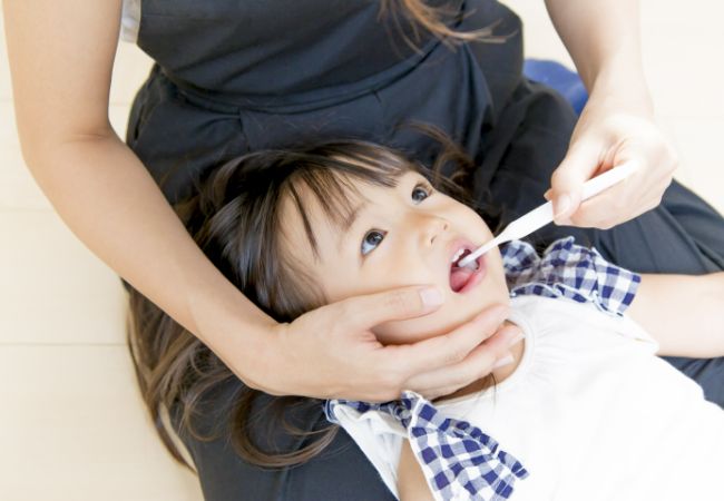 膝の上で歯磨きをしてもらう口をあけた女の子