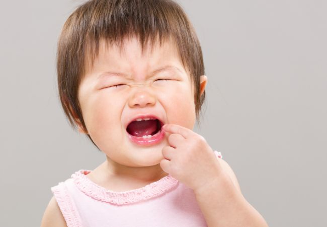 泣きながら口元を触る乳児